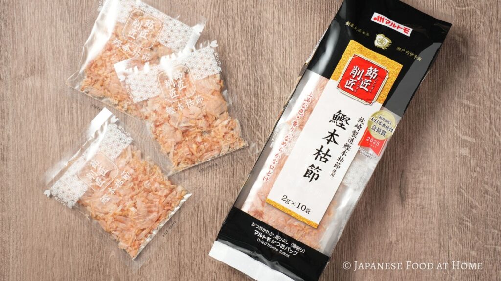 Small packets of dried bonito flakes and a package of bonito flakes on a wooden table.