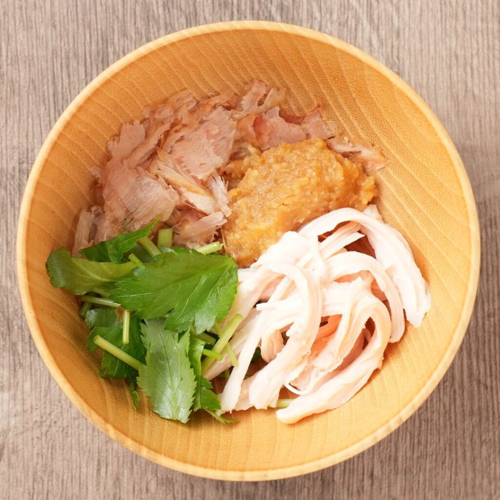 Kachuyu ingredients in a wooden bowl with bonito flakes, miso, chicken, and mitsuba.