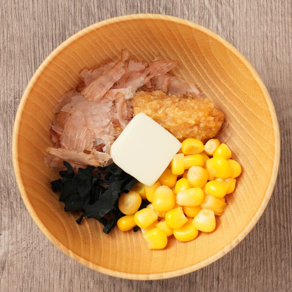 Kachuyu ingredients in a wooden bowl with bonito flakes, miso, corn, wakame, and butter.