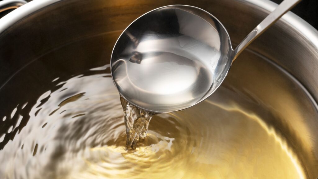 Clear Japanese dashi soup stock being scooped from a pot with a ladle.