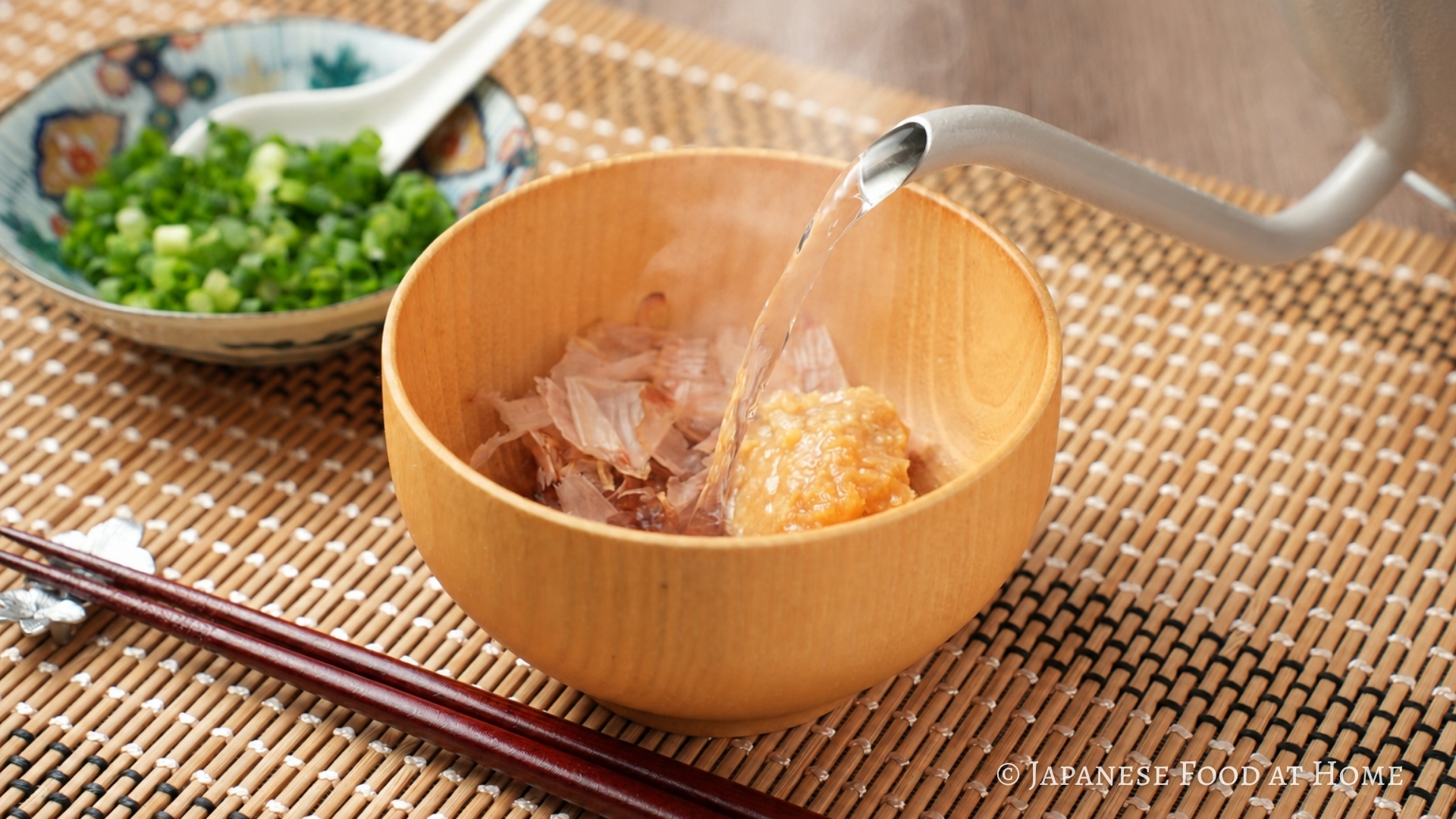 Hot water being poured over miso and bonito flakes in a wooden bowl to make kachuyu, an Okinawan miso soup.