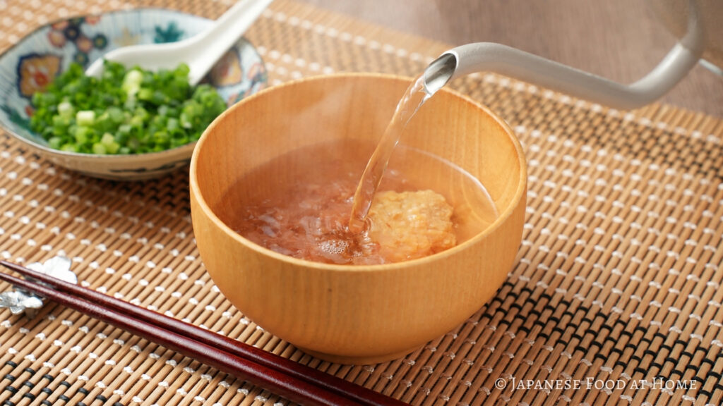 Hot water being poured over miso and bonito flakes in a wooden bowl to make kachuyu.