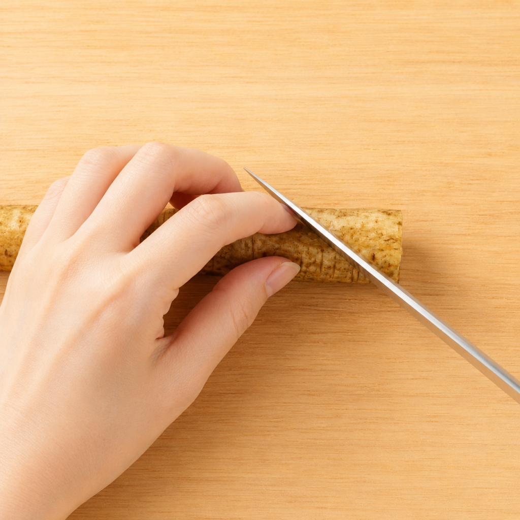 Burdock root being cut diagonally to begin rangiri on a wooden cutting board