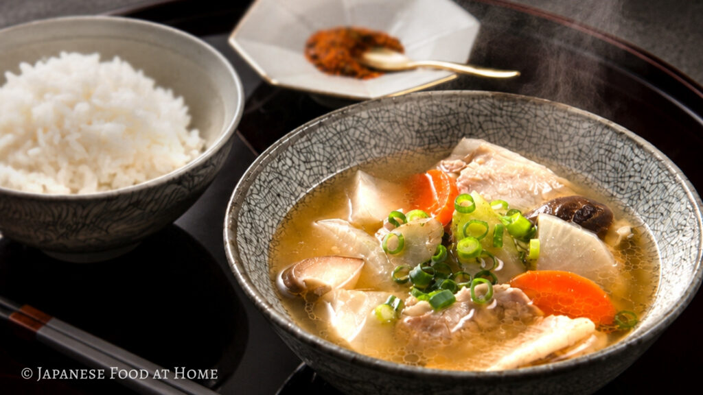 Tonjiru pork miso soup with rice, shichimi, and chopsticks served on a Japanese lacquer tray.