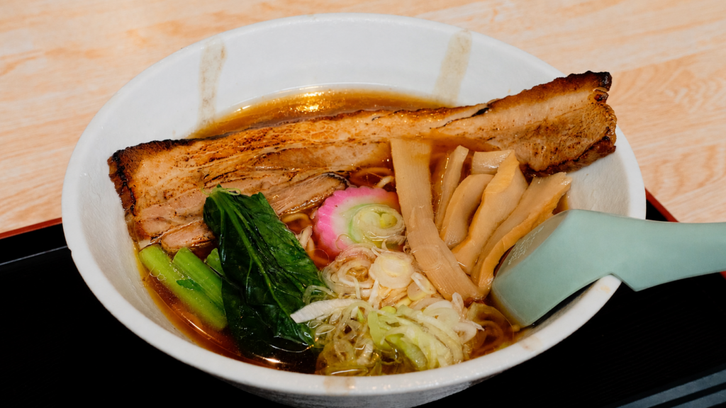 Pork shoyu ramen at Kuidokoro Akashi in Kamikawa, Hokkaido, topped with grilled pork, bamboo shoots, greens, narutomaki, and Japanese leek.