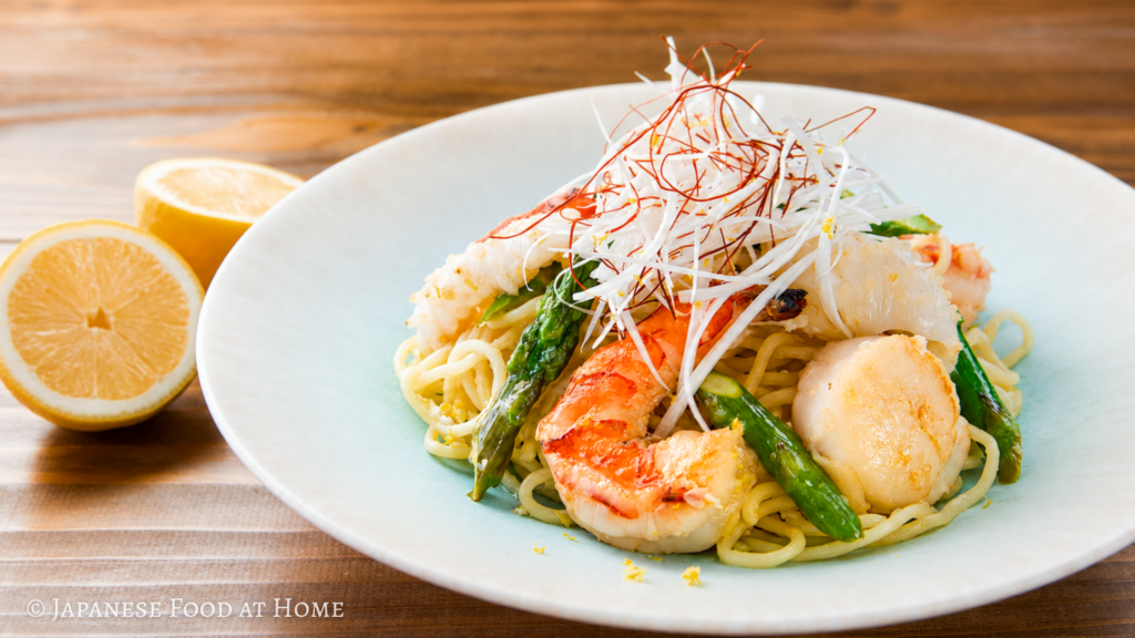 Seafood yakisoba with shrimp, scallops, asparagus, lemon, and white leek garnish on a white plate