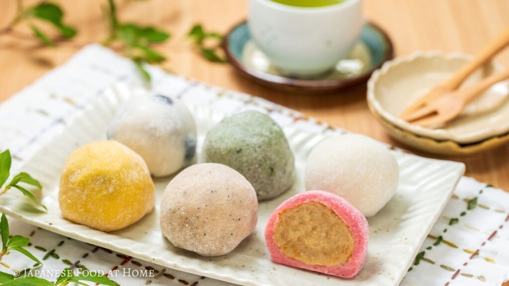 An assortment of colorful daifuku from Mochigoya Mam in Kamikawa, Hokkaido, with one pink daifuku cut open to show the filling