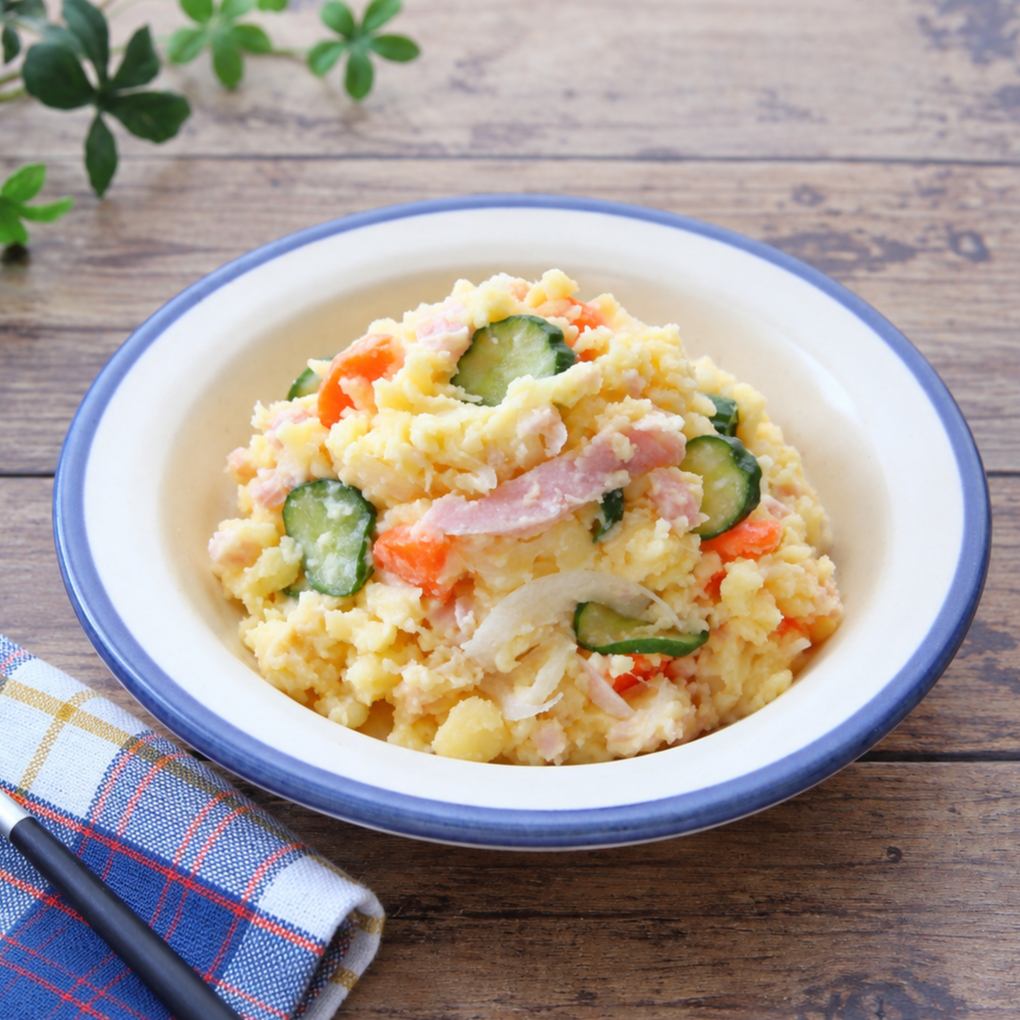 Japanese potato salad with chunky mashed potatoes, cucumber, carrots, and ham, served in a white bowl with a blue rim.