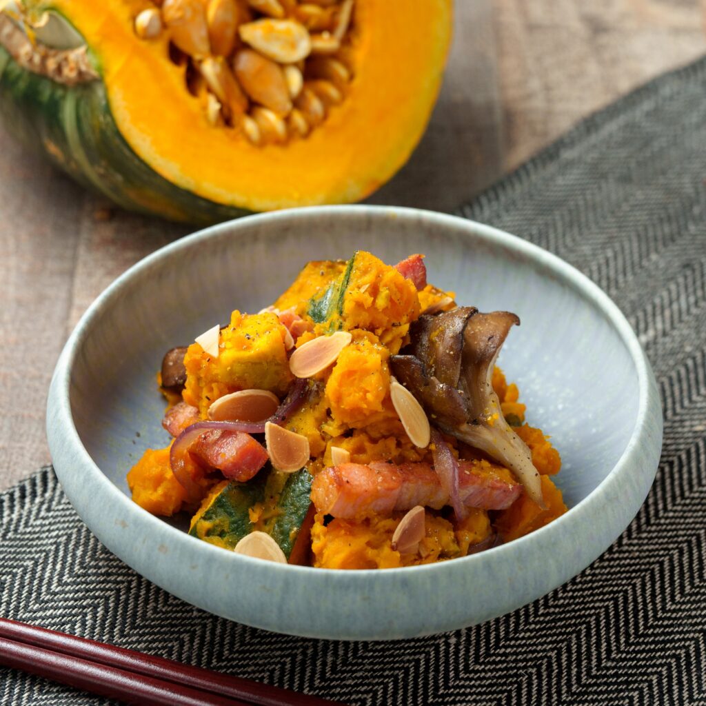 Japanese-style kabocha salad with bacon, maitake mushrooms, and sliced almonds, served in a ceramic bowl with fresh kabocha squash in the background.